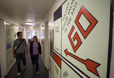 Two students walking down a residence's hallway and the walls are painted like Monopoly squares.