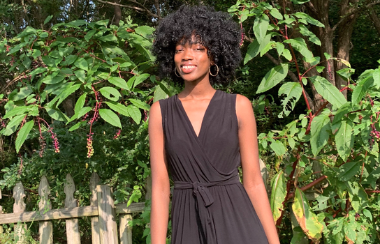 Ayooluwa smiling and standing in front of a fence and lush greenery.