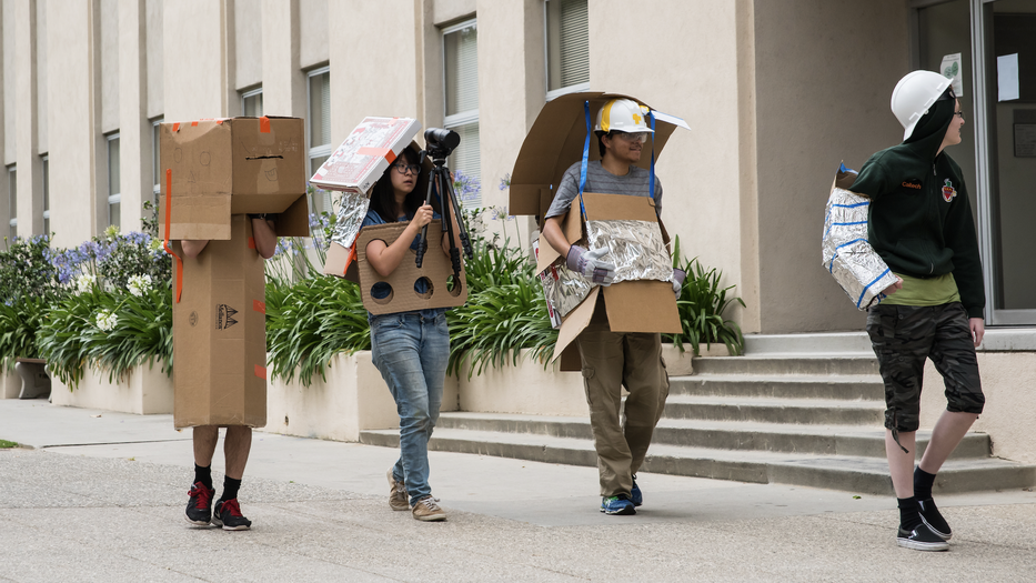 Four students with props walking in a line during Ditch Day