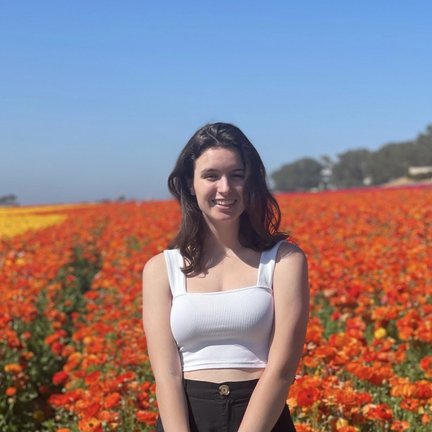 Profile photo of Isabel standing in front of a field of flowers on a cloud-free day