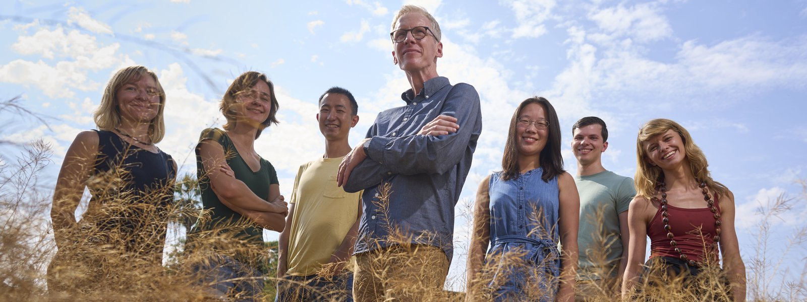 group of 7 people standing smiling in a field of grass
