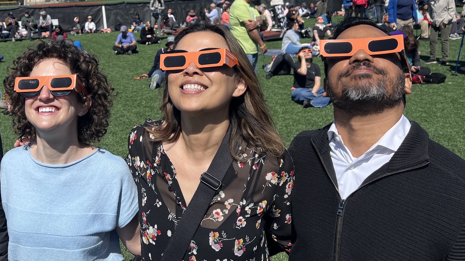 Three people with orange glasses looking up during an eclipse