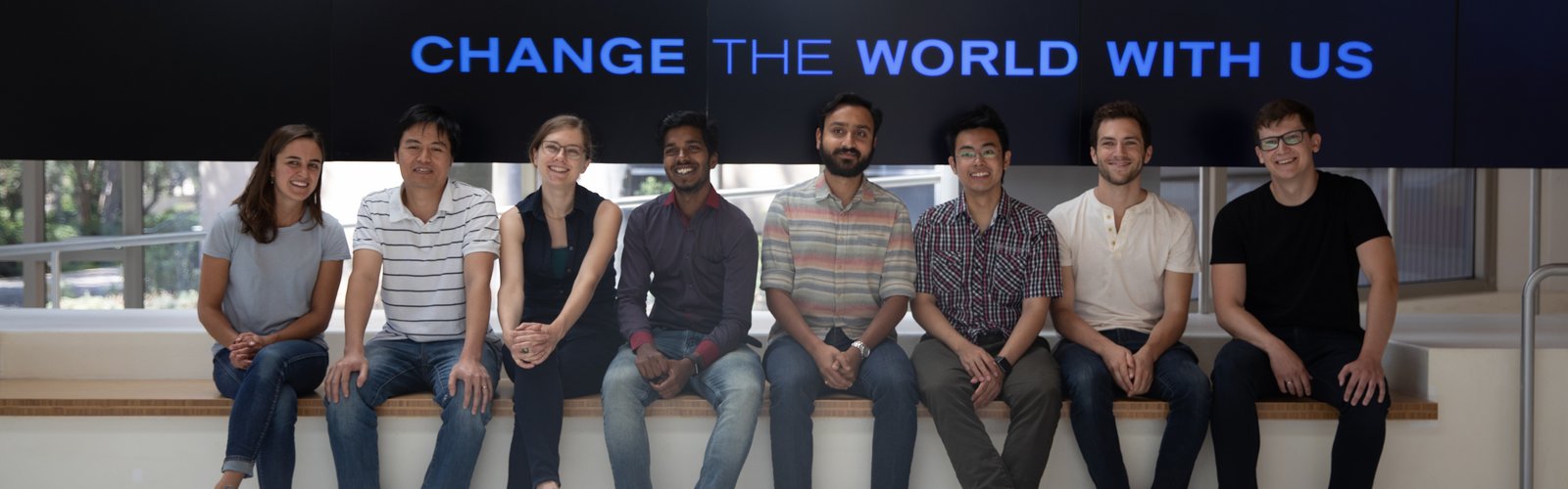 Group of 8 people sitting on a bench smiling