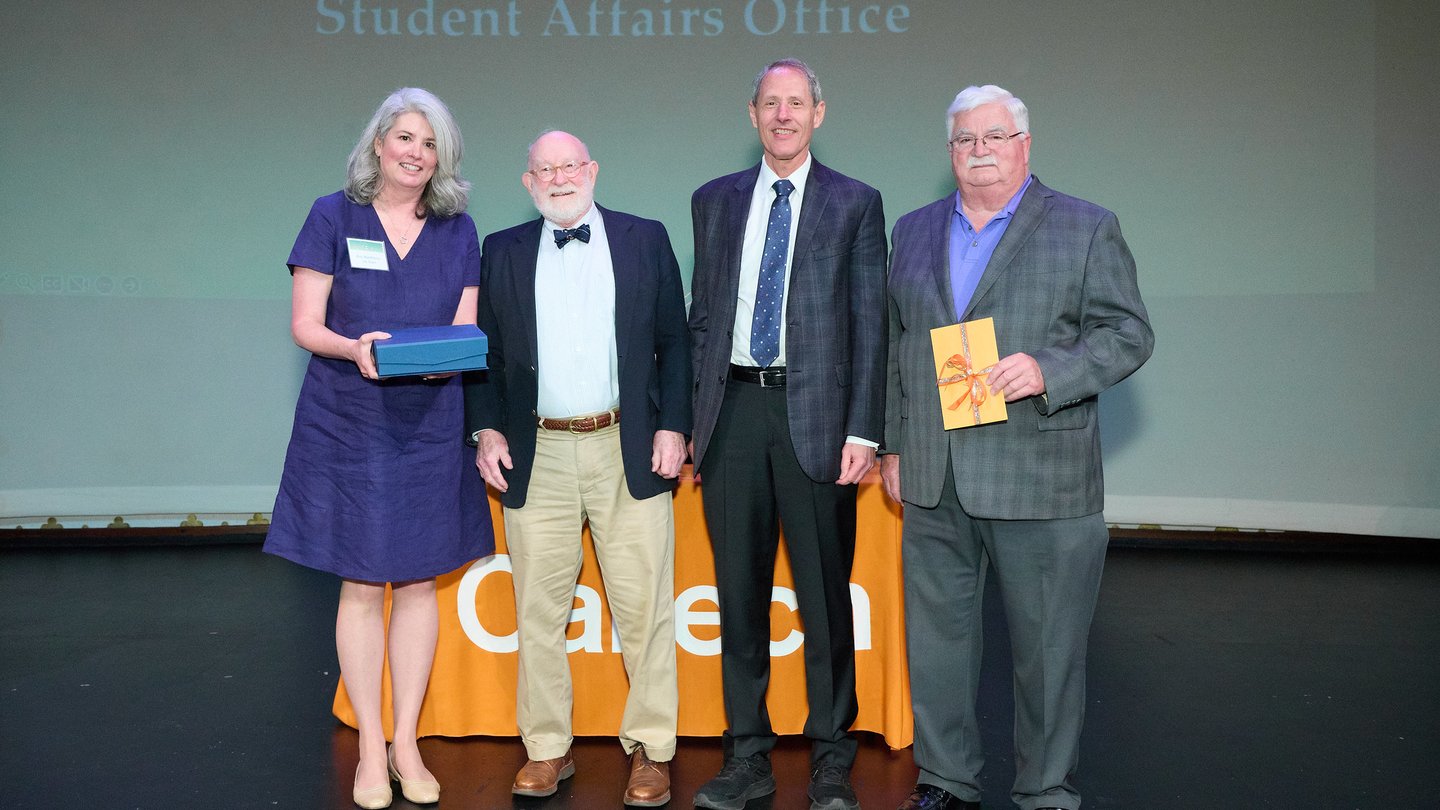 Four people on a stage. L to R Kim Mawhinney, Thomas W. Schmitt, Thomas F. Rosebaum, Ted Jenkins