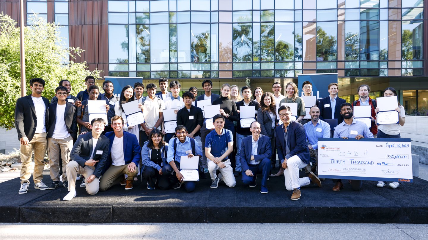Caltech students, entrepreneur Bill Gross, and representatives from Sunstone Management and American Lending Center kneeling and standing on a stage, smiling. Students are holding certificates they've won from the competition.