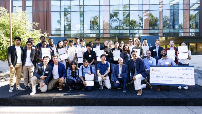 Caltech students, entrepreneur Bill Gross, and representatives from Sunstone Management and American Lending Center kneeling and standing on a stage, smiling. Students are holding certificates they've won from the competition.