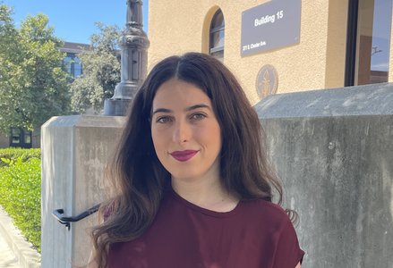 Young woman with dark hair, wearing dark magenta lipstick and a burgundy top