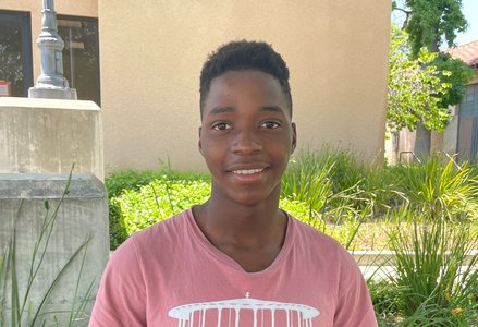 Young Black man with short hair wearing a salmon T-shirt smiling in front of a terracotta building