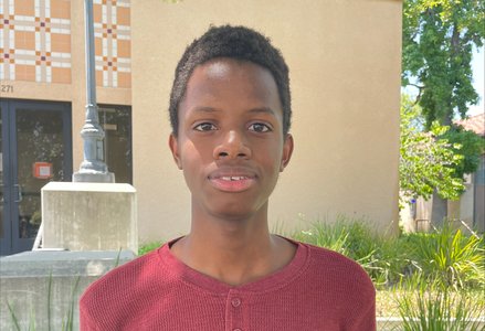 Young Black man with short hair wearing a burgundy henley smiling in front of a terracotta building