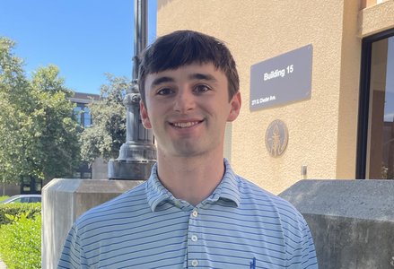 Clean-shaven young man with medium brown hair wearing a light blue horizontal stripe polo shirt