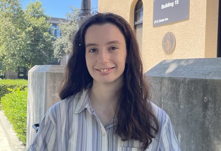 Young woman with slightly past shoulder length medium brown hair, blue and white vertical stripe short sleeved button-down