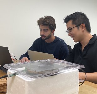 Two young men sitting in front of a laptop, smiling.