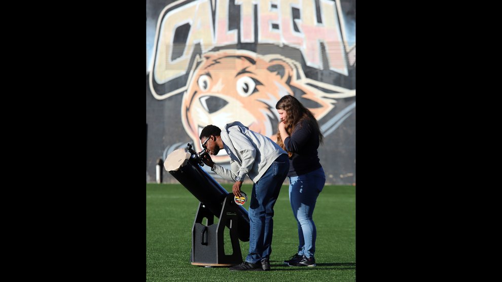 A man and woman set up a telescope on the athletic field