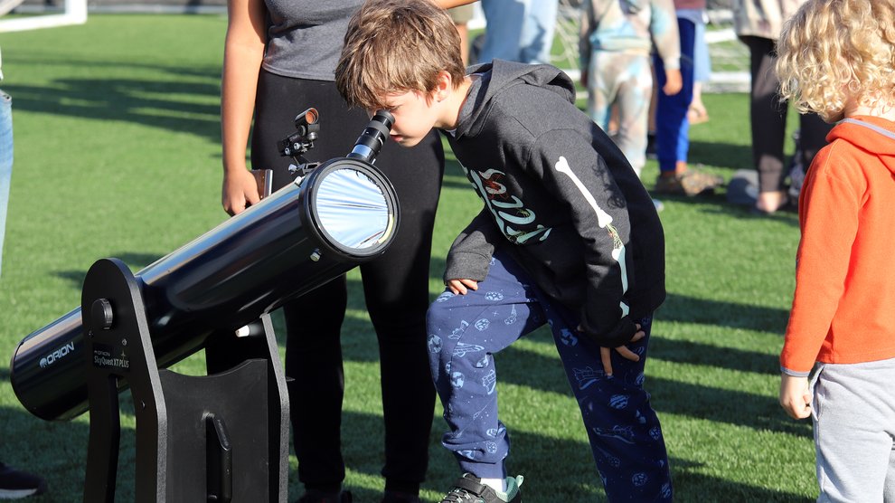 a young boy peers into the eyepiece of a telescope