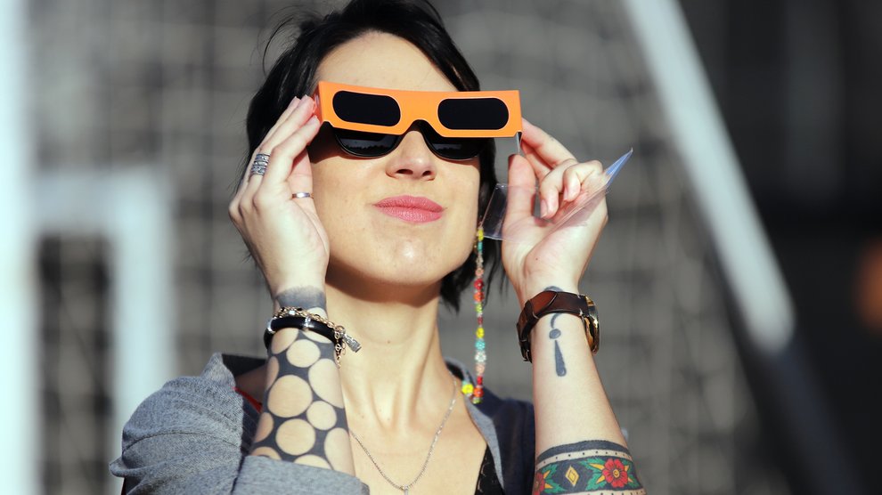 A woman peers through solar glasses at the sky
