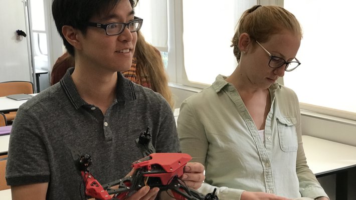 Students examine a 3D printed drone and a round component designed to hold a stylized table's legs in place.