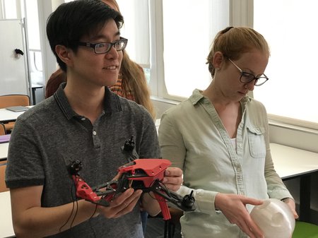 Students examine a 3D printed drone and a round component designed to hold a stylized table's legs in place.