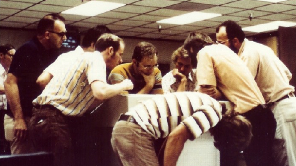 The CRS team gets its first look at the Voyager 2 data in 1977. Cummings is bent over in the foreground, reading data upside down as it emerges from the printer.