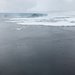 A large block of ice in the distance, ocean in the foreground. A cylindrical instrument hangs in frame at the lower right.