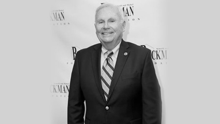 A black-and-white photo of Bill May wearing a suit and smiling.