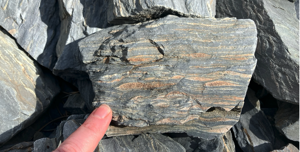 A person's finger points to stripes on a rock