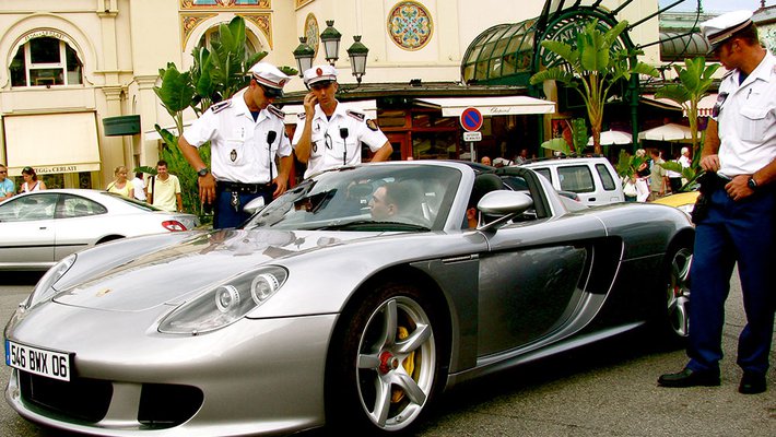 Two men sit in a Porsche while a police officer talks to them. A few more officers stand nearby, looking on.