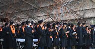Students in caps and gowns celebrate commencement as orange confetti flies in the air.