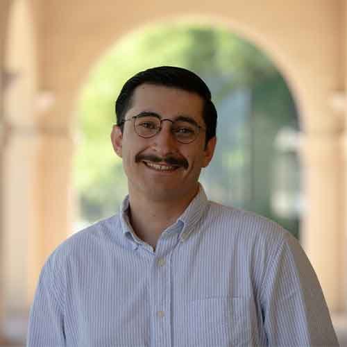 person in glasses posing in front of arches outdoors