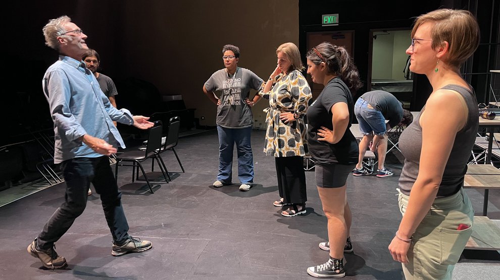 Brian Brophy faces a group of four cast members on a stage