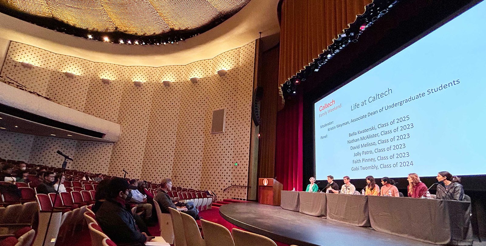 Parents in the first two rows of an auditorium look to the stage, where a panel of students sit in front of a screen that says "Life at Caltech"