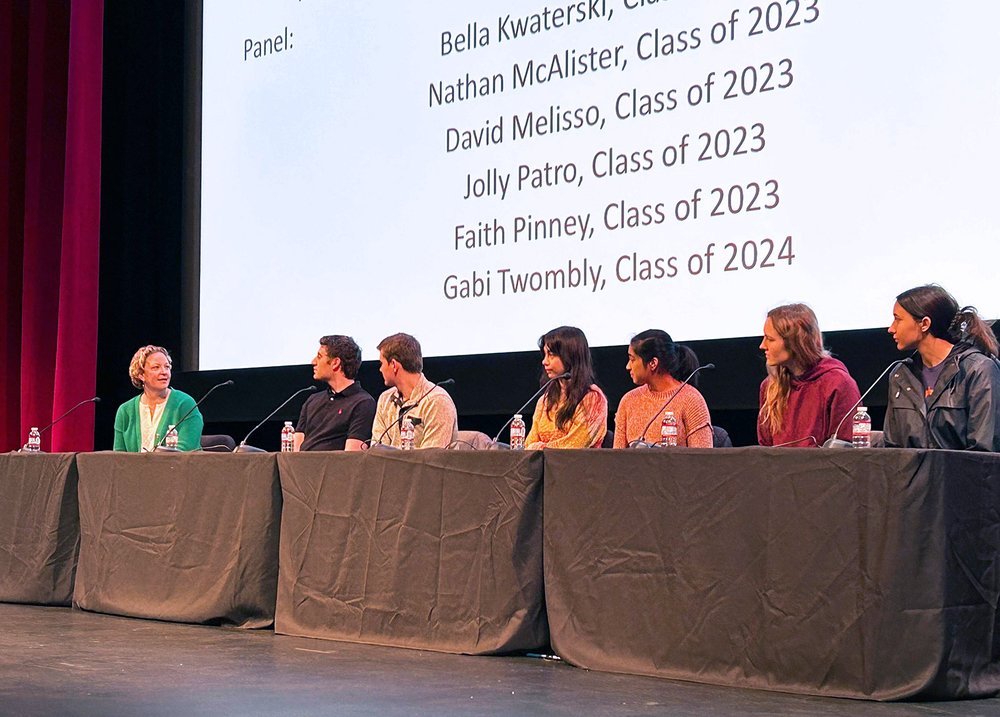 A panel of students sit behind a table on stage.