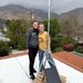 Two women stand behind a particulate air quality sensor mounted like a tripod on a roof in front of stormy looking mountains.