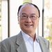 A portrait of Thomas Hou. He wears as suit and glasses and smiles at the camera.