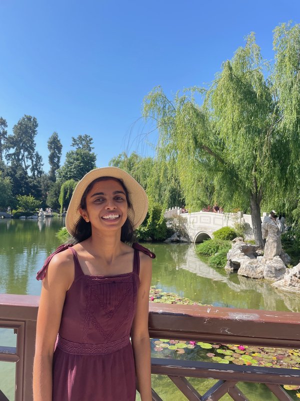 A woman in a hat stands smiling for a photo outdoors.