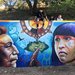 mural painting on a wall with an indigenous man, a tree, the sun above, and an indigenous girl