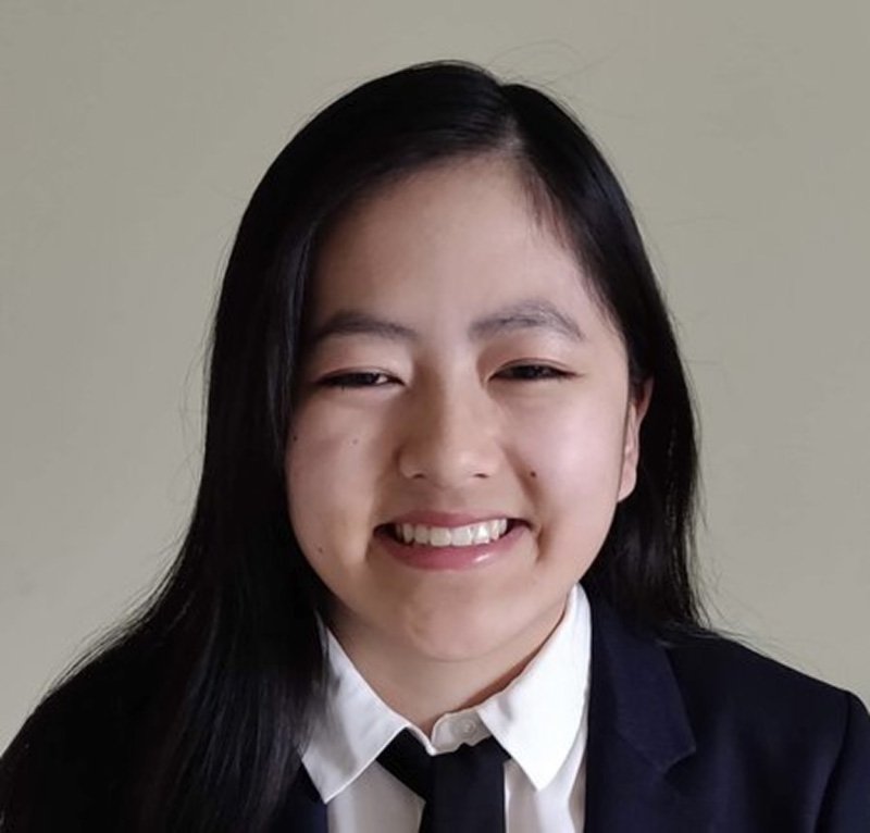 A young woman with long dark hair wearing a suit smiles at the camera