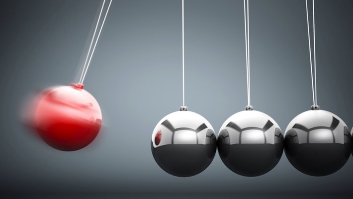 A Newton's cradle toy is shown with the far left, red ball in movement, headed toward hitting the next silver ball.