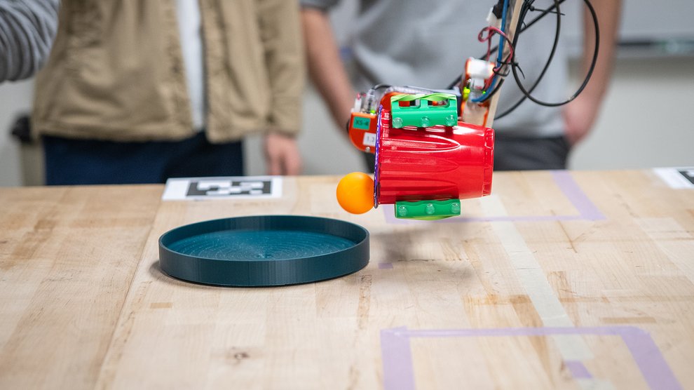 A robotic arm has poured an orange ping pong ball out of a red plastic cup.