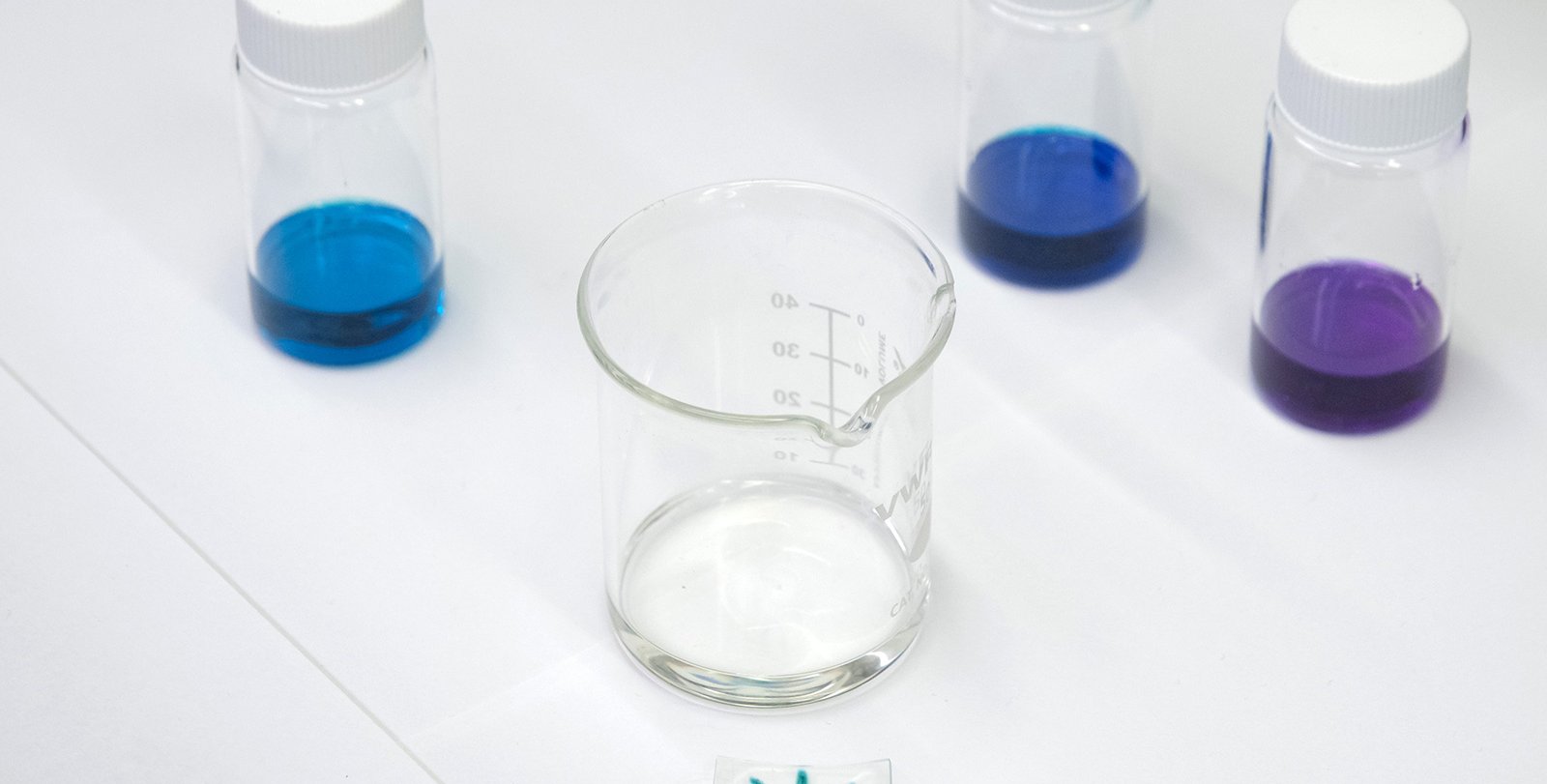 A thin piece of plastic with a colored radial pattern sits on a work bench surrounded by glass vials of brightly colored dyes.