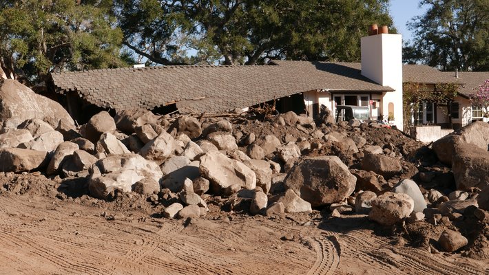 Photo of a house damaged by large boulders and rocks of varying sizes