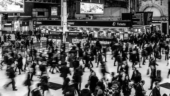 A black-and-white photograph of a crowd of people moving through a train station.