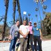 Two women and two men pose with an air quality monitoring sensor on a roof with burned trees in the background.