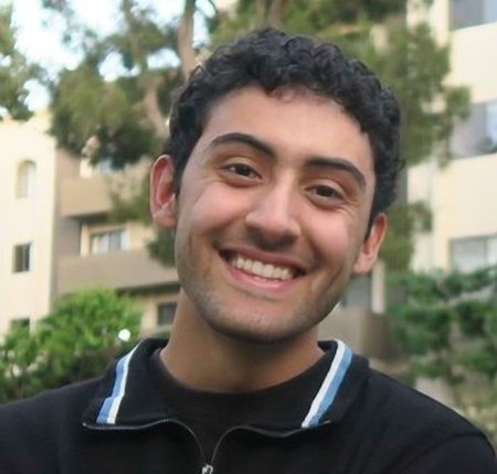 A young man with curly dark hair smiles at the camera