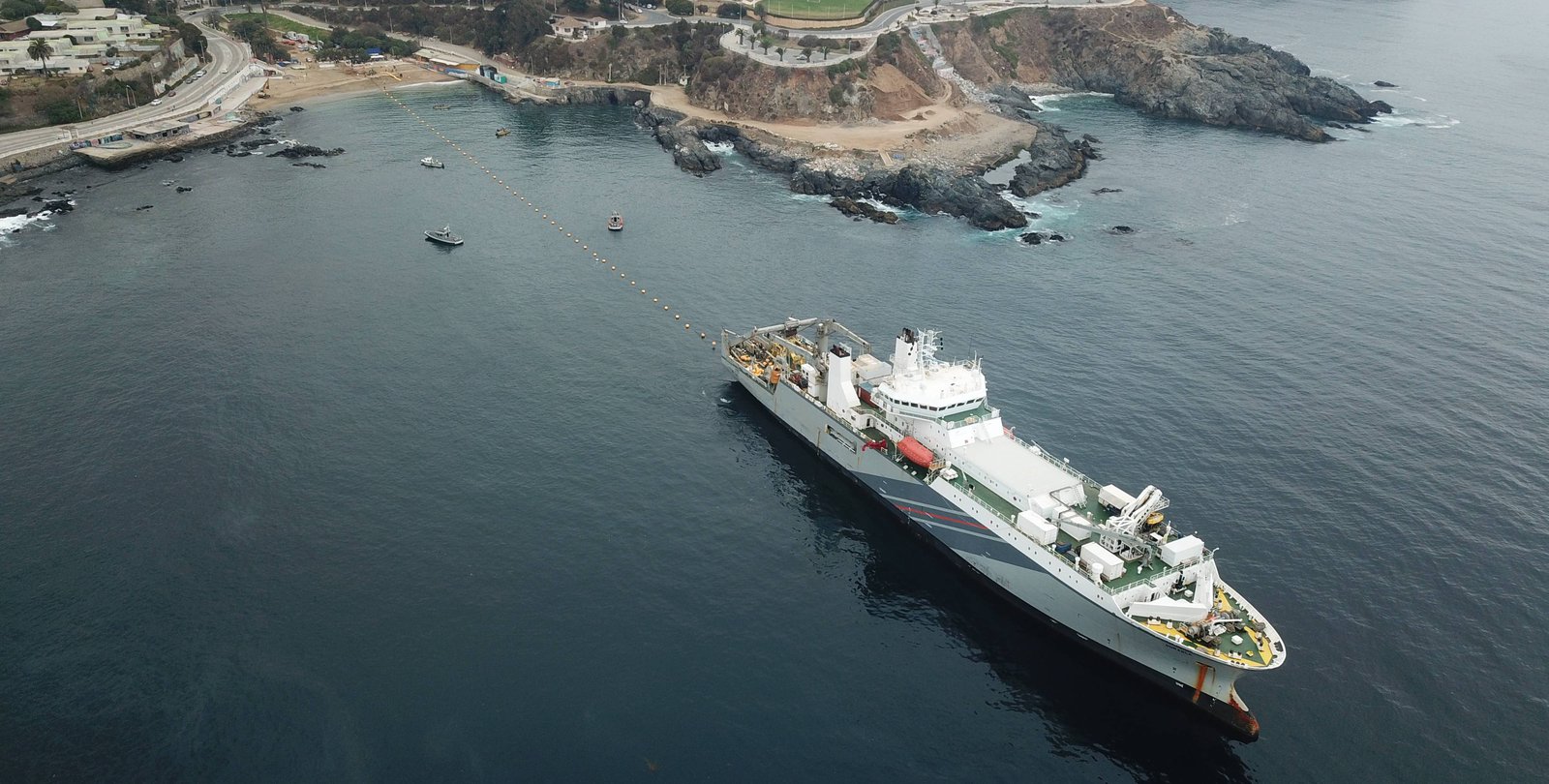 A ship, bottom right, steams out from shore unspooling the Curie cable