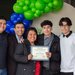 Five people smile for the camera in front of balloons, while holding a certificate