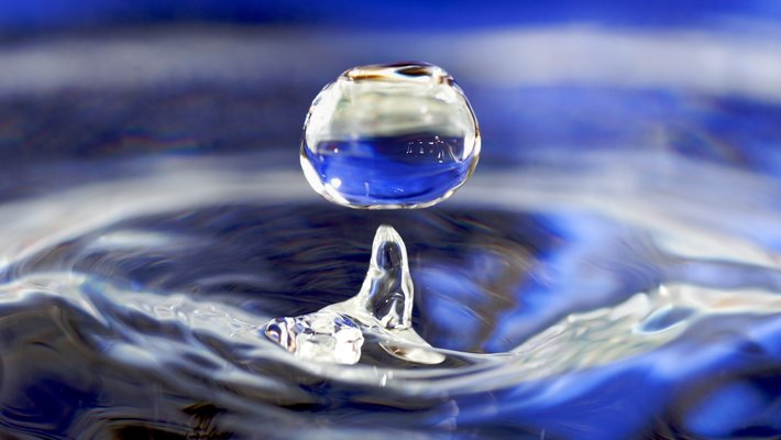 A drop of water splashes up out of a larger body of water