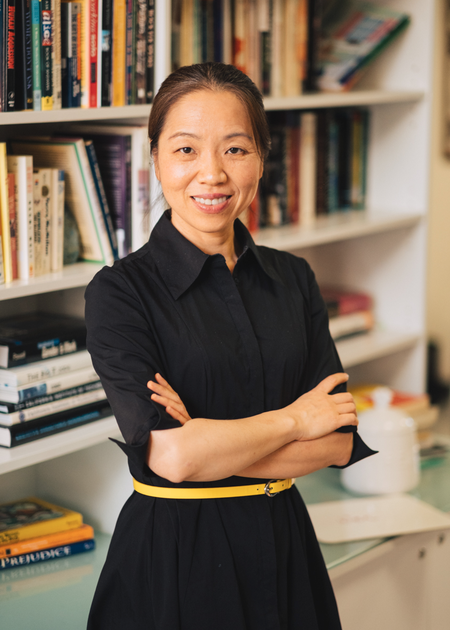 A photo of Wen Chen with her arms crossed in front of a bookshelf