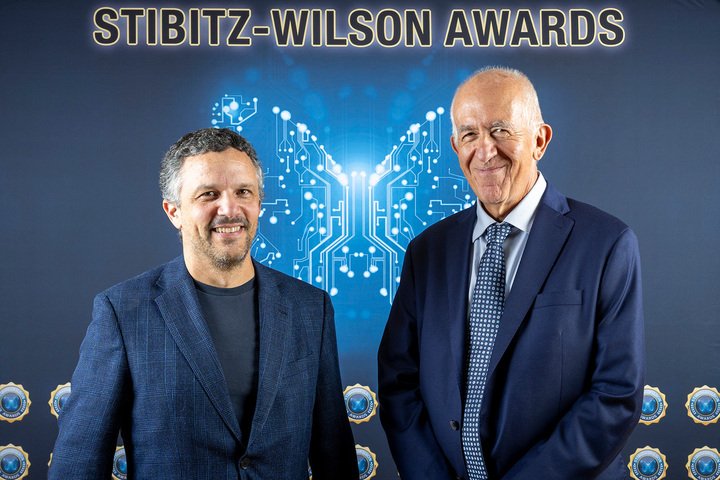 two men in suits in front of a Wilson-Stibitz Awards background featuring computer schematics in the shape of a butterfly