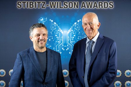 two men in suits in front of a Wilson-Stibitz Awards background featuring computer schematics in the shape of a butterfly
