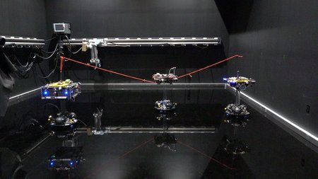 Two spacecraft in a black lab space are connected by a reddish tether. A third spacecraft is captured in the center of the tether.